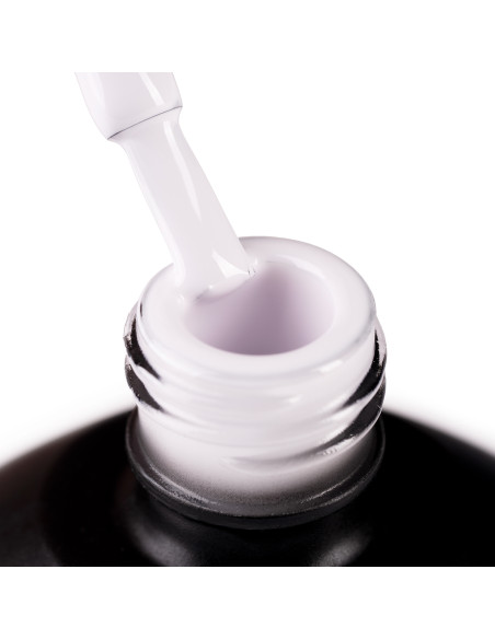 Szyjka butelki i oparty o nią pędzelek zanurzony w mlecznym beżowym odcieniu lakieru hybrydowego