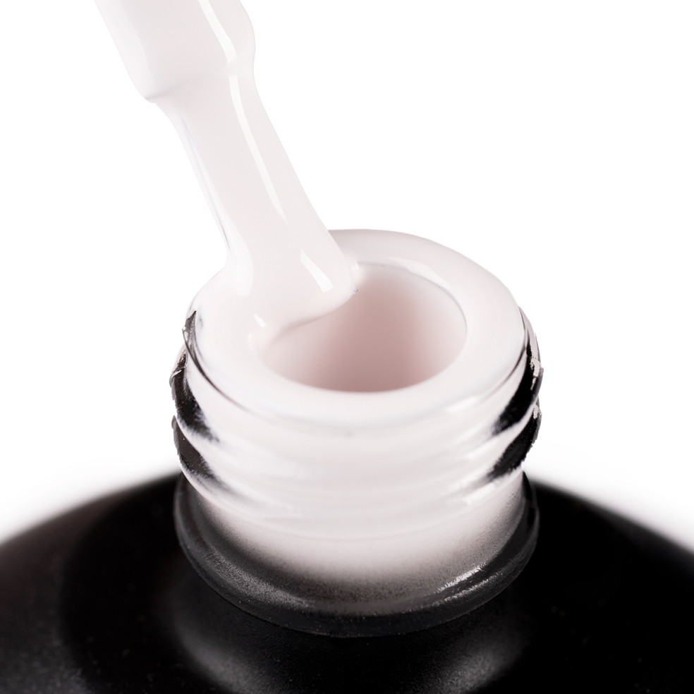 Szyjka butelki i oparty o nią pędzelek zanurzony w jasnym, ciepłym odcieniu beżowego lakieru hybrydowego