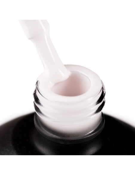 Szyjka butelki i oparty o nią pędzelek zanurzony w jasnym, ciepłym odcieniu beżowego lakieru hybrydowego