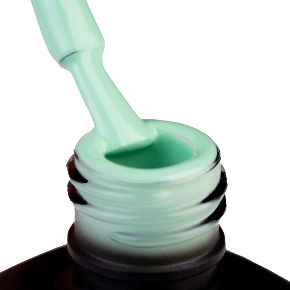 Szyjka butelki i oparty o nią pędzeleke zanurzony w lakierze hybrydowym w kolorze miętowym szałwiowym zielonym