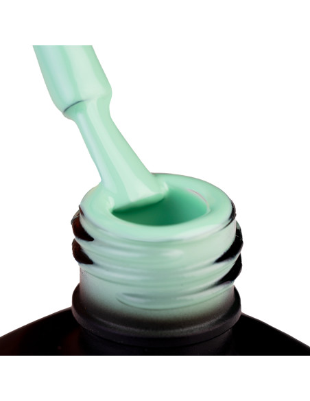 Szyjka butelki i oparty o nią pędzeleke zanurzony w lakierze hybrydowym w kolorze miętowym szałwiowym zielonym