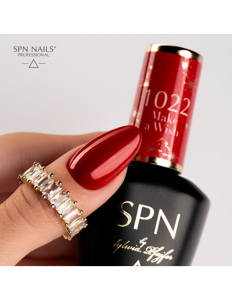 Butelka z lakierem hybrydowym i kciuk pomalowany czerwonym lakierem hybrydowym z drobinkami