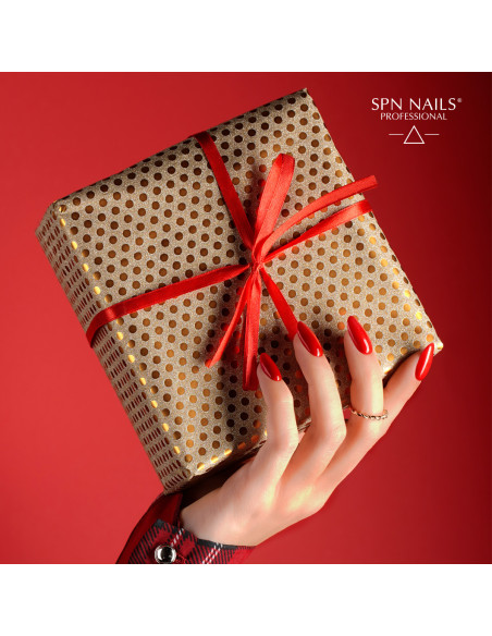 Dłoń trzymająjca zapakowany prezent. Paznokcie pomalowane lakierem hybrydowym w kolorze czerwonym z drobinkami