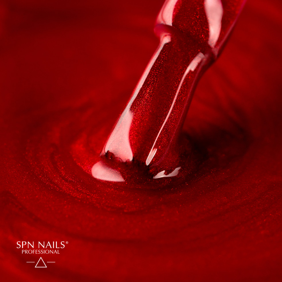 Lakier hybrydowy w kolorze czerwonym z drobinkami i zanurzony w nim pędzelek