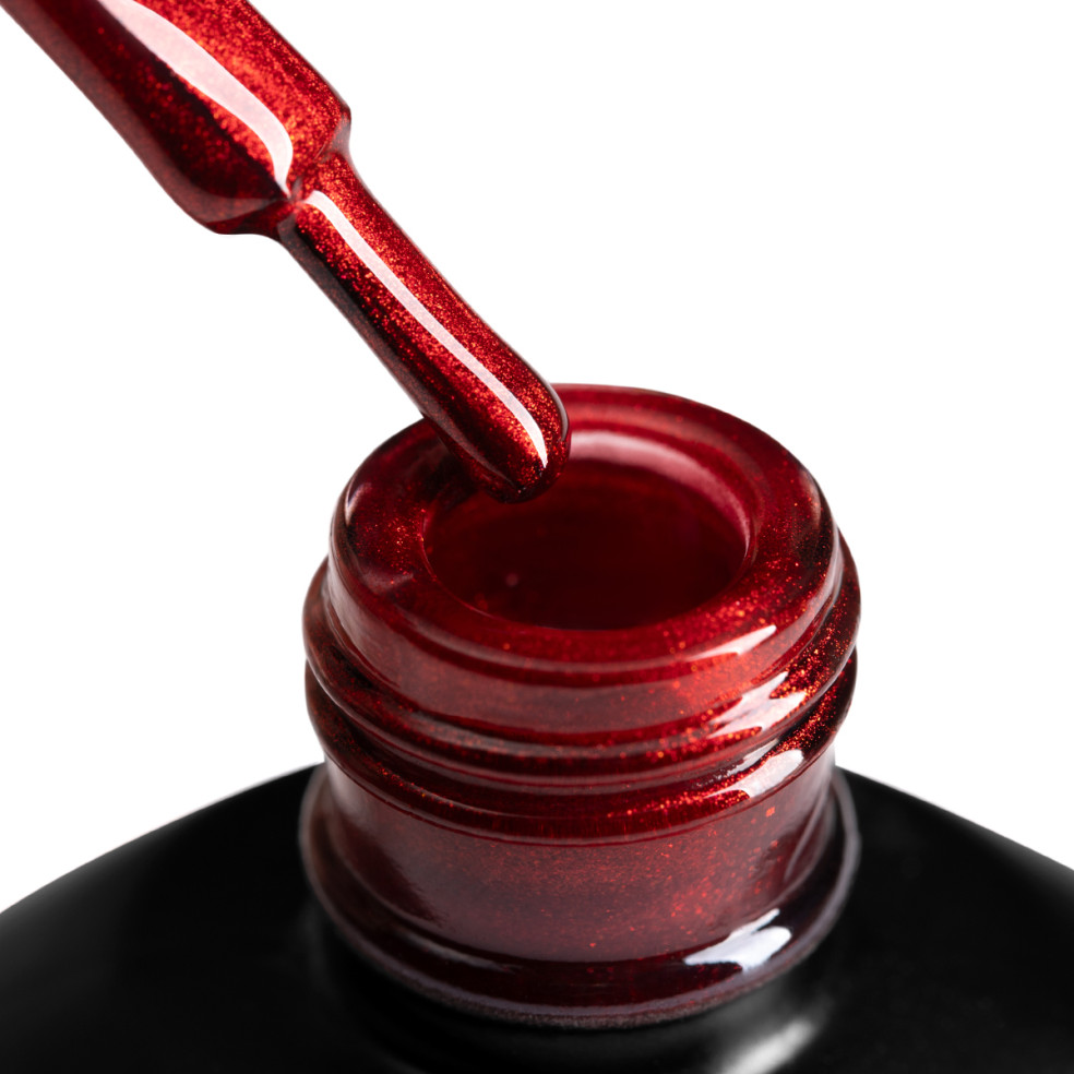 Szyjka butelki z lakierem hybrydowym i oparty o nią pędzelek, zanurzony w czerwonym metalicznym lakierem hybrydowym