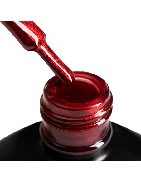 Szyjka butelki z lakierem hybrydowym i oparty o nią pędzelek, zanurzony w czerwonym metalicznym lakierem hybrydowym