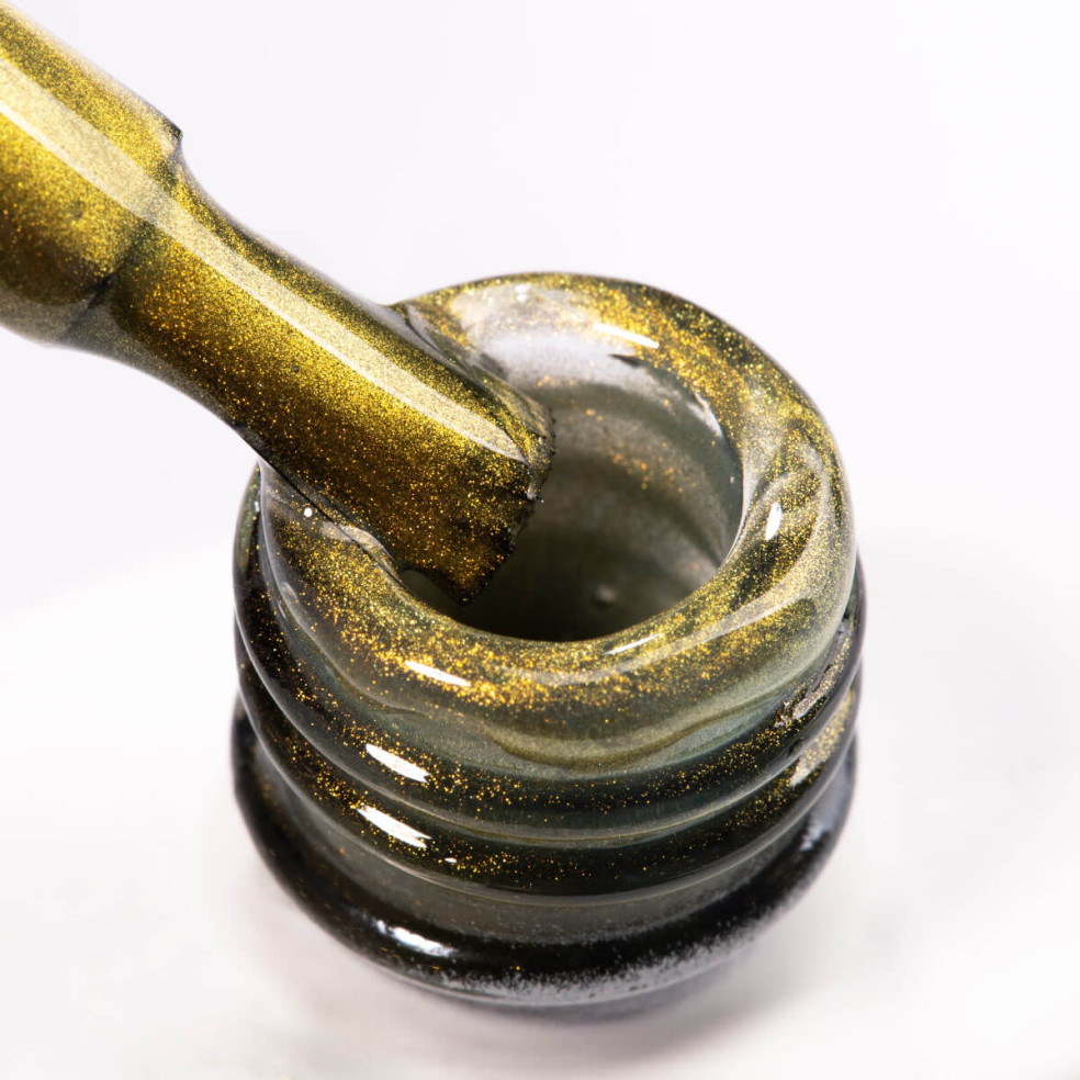 Szyjka butelki i pędzelek zanurzony w złotym lakierze hybrydowym z efektem cat eye Szyjka butelki i pędzelek zanurzony w złotym lakierze hybrydowym z efektem cat eye