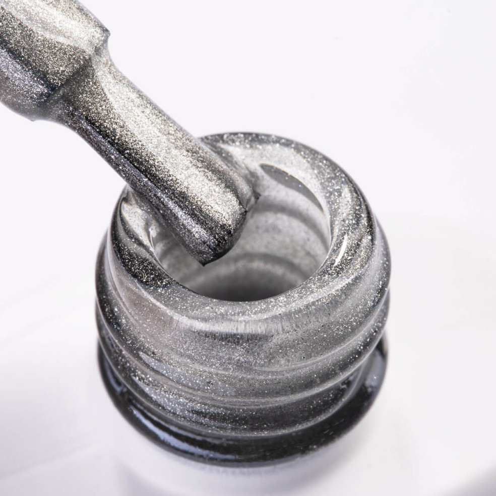 Szyjka butelki i pędzelek zanurzony w srebrnym lakierze hybrydowym z efektem cat eye Szyjka butelki i pędzelek zanurzony w srebrnym lakierze hybrydowym z efektem cat eye