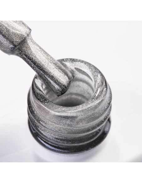 Szyjka butelki i pędzelek zanurzony w srebrnym lakierze hybrydowym z efektem cat eye Szyjka butelki i pędzelek zanurzony w srebrnym lakierze hybrydowym z efektem cat eye