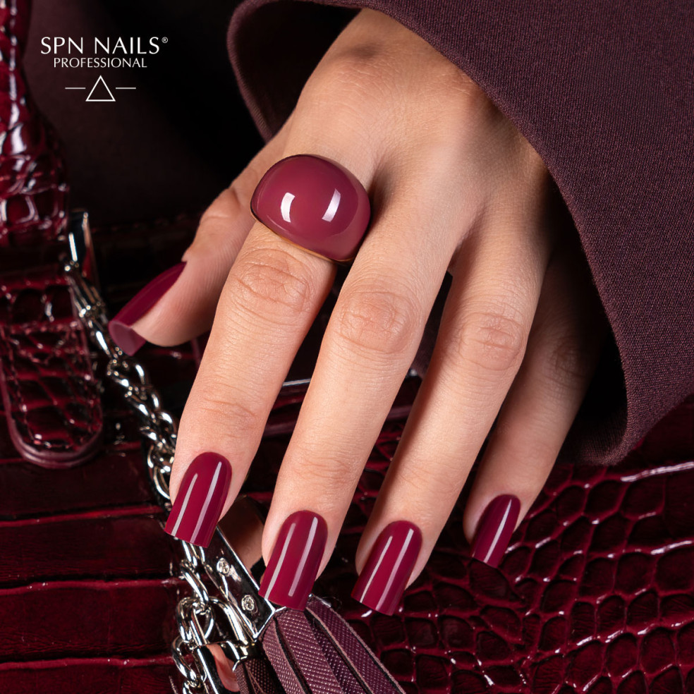 Bordowy manicure lakierem hybrydowym 1044 Guilty Pleasures z zestawu Dark Desires SPN Nails na dłoni trzymającej torebkę