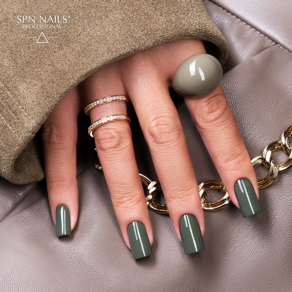 Zielony manicure lakierem hybrydowym 1047 Scandalous z zestawu Dark Desires SPN Nails na dłoni ze złotymi pierścionkami